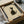 May include: Framed minimalist cat artwork in black frame, being unboxed from brown cardboard packaging with protective wrapping. The print shows a simple black and white illustration of a sitting cat looking upward against a beige background, with a small red stamp mark in the corner. Wooden dowels and tissue paper are visible around the frame on a white surface.