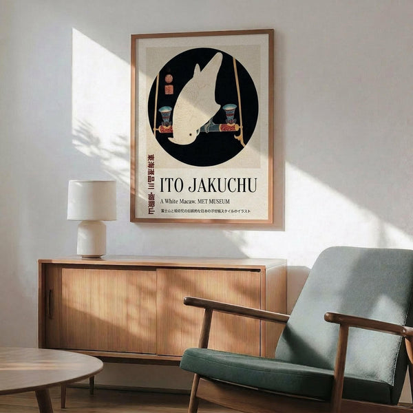 May include: Framed poster featuring a white macaw in a black circle with Japanese text below, displayed above a wooden credenza with ceramic lamp in a mid-century modern living room. Green upholstered chair with wooden frame sits nearby on light wood floors with natural sunlight streaming across white walls.