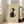 May include: Large framed poster displaying minimalist black and white cat artwork in Japanese ink painting style, leaning against white wall next to beige upholstered sofa. The cat sits with head tilted upward, featuring bold black and cream brushstrokes on textured beige background with small red seal mark. Natural light streams through windows in bright, airy living room setting.