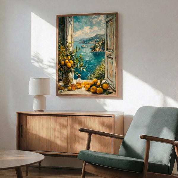 May include: Framed Mediterranean coastal artwork showing open window view of turquoise sea, mountains, and citrus fruits on windowsill, displayed above wooden sideboard with white lamp in modern living room with mint green armchair and natural lighting creating geometric shadows on white wall.