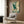 May include: Japanese-style artwork featuring a blue-green heron with outstretched wings flying through stylized cream and teal clouds, displayed as a framed print on wood-paneled wall above a beige upholstered armchair with geometric patterned pillow, alongside a brass floor lamp and dark round side table with open book in a modern neutral-toned room setting.