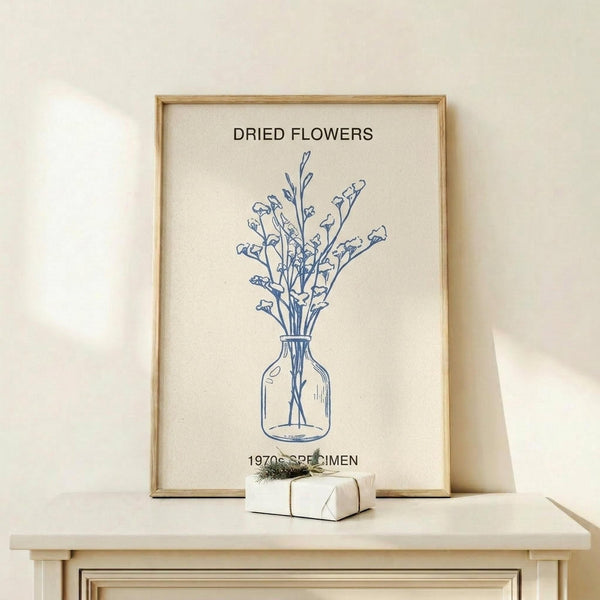 May include: Framed botanical line drawing print in light wood frame showing dried flowers in glass vase, displayed on pale wood shelf against cream wall. Blue ink illustration on textured cream paper with "DRIED FLOWERS" and "1970s SPECIMEN" text. Small wrapped gift box with greenery sits beside frame. Minimalist Scandinavian-style home decor setting with soft natural lighting.