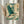 May include: Framed Japanese-style artwork depicting a blue-green heron in flight with outstretched wings soaring through stylized cream and teal clouds. The print features traditional ukiyo-e inspired waves and swirling cloud patterns with a red text cartouche in the upper right corner. Displayed in a light wooden frame on a neutral wall beside dried pampas grass stems and flowing curtains in soft natural lighting.
