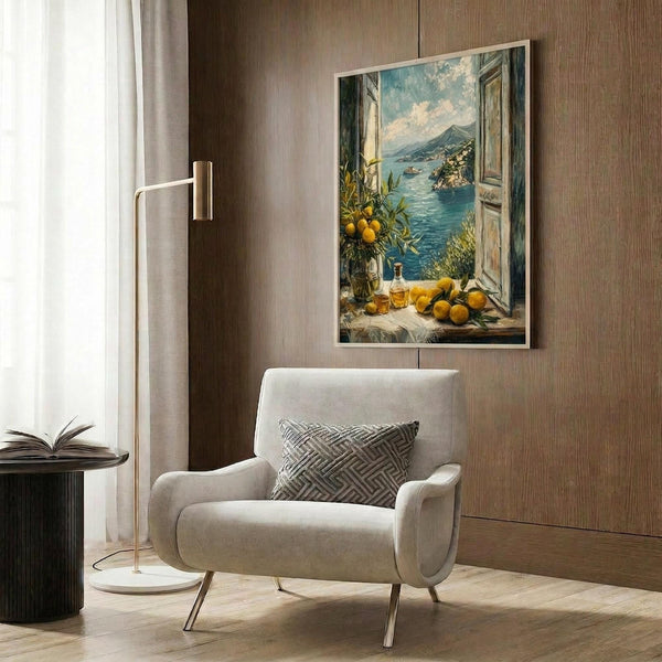 May include: Mediterranean coastal artwork displayed in modern living room with beige armchair, brass floor lamp, and wood paneled wall. The framed print shows an open window view of turquoise waters, mountains, and lemon branches with oranges and bottles on the windowsill. Warm natural lighting creates cozy reading nook atmosphere.
