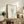 May include: Framed botanical wall art displaying blue line drawing of dried flowers in a glass vase, positioned on rustic wooden sideboard alongside fern plant, books, ceramic pottery, and brown leather furniture in neutral-toned living room setting