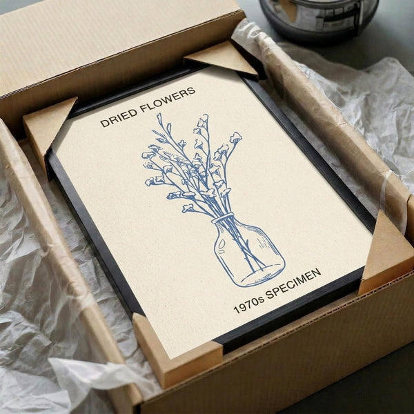 May include: Vintage-style botanical print in black frame showing line drawing of dried flowers in a vase, displayed in cardboard shipping box with tissue paper protection. Cream-colored poster features blue ink illustration with "DRIED FLOWERS" and "1970s SPECIMEN" text. Minimalist scientific specimen aesthetic with simple vase containing delicate stem flowers.