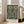 May include: Framed poster with William Morris floral pattern in dark navy background featuring ornate golden flowers, green leaves, and intricate white botanical details. Light wood frame leans against white wall next to beige upholstered chair in bright room with large windows and natural lighting on hardwood floors.