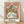 May include: A framed Picasso-style cubist portrait showing a seated woman with geometric features in green, yellow and pink tones against a coral background, displayed in a light wood frame on wooden flooring against white walls with natural lighting creating soft shadows.