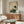 May include: Japanese-style artwork featuring a white stork with black wing tips standing beside a turtle, surrounded by green foliage and Asian calligraphy on aged beige background. Displayed in thin wooden frame above mid-century walnut credenza in modern living room with white curved chair, brass floor lamp, and oval glass coffee table.
