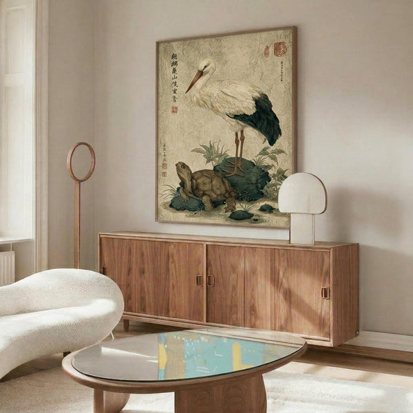 May include: Japanese-style artwork featuring a white stork with black wing tips standing beside a turtle, surrounded by green foliage and Asian calligraphy on aged beige background. Displayed in thin wooden frame above mid-century walnut credenza in modern living room with white curved chair, brass floor lamp, and oval glass coffee table.