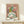 May include: Framed Picasso-style cubist portrait print displayed on light wood shelf against cream wall. Artwork features abstract female figure with green and yellow tones, geometric shapes, and pink background. Thin wood frame surrounds the poster. Small white wrapped gift box with natural twine and pine sprig sits on shelf beside the frame.
