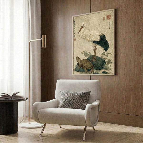 May include: Traditional Japanese-style artwork featuring a white stork with dark wing feathers standing on a turtle, surrounded by green foliage, displayed in a light wooden frame against wood paneled walls in a modern living room with beige armchair, brass floor lamp, and dark side table