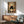 May include: Framed poster displayed above a wooden credenza in a modern living room with mint green chair and white lamp. The artwork shows a black cat with large white eyes sitting behind a bowl of ramen noodles with a bottle, set against a collage background of vintage Japanese text and imagery in warm earth tones.