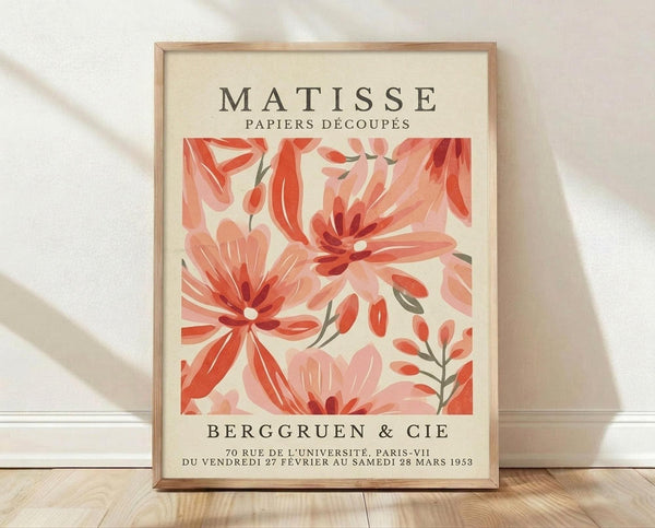 May include: Framed vintage-style art print with coral and pink floral cut-out designs in Matisse's paper collage style, displayed in light wood frame against white textured wall on wooden floor with soft natural lighting and shadows