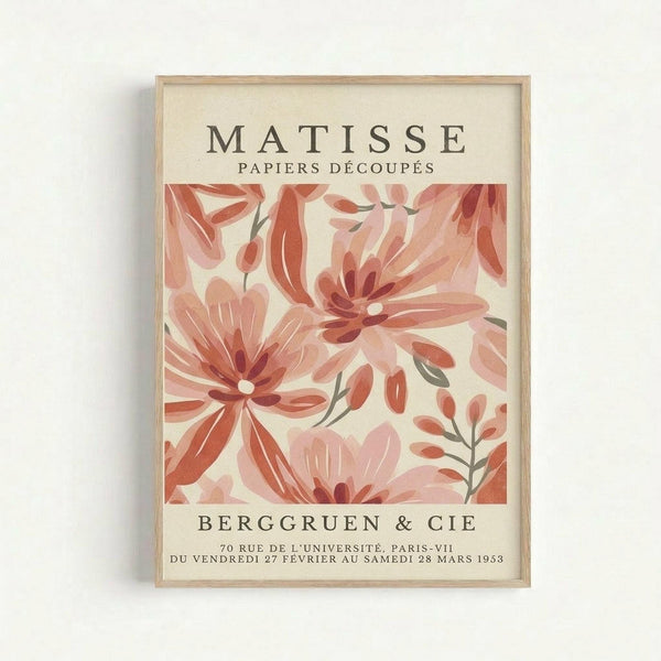 A framed vintage exhibition poster featuring abstract floral cutout designs in coral, pink, and salmon tones against a cream background. The artwork displays flowing organic shapes resembling magnolia blooms and botanical elements. Text reads "MATISSE PAPIERS DÉCOUPÉS" at top and "BERGGRUEN & CIE" with Paris gallery details and 1958 dates below. The poster is displayed in a light wood frame against a white wall.