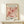 May include: Framed vintage-style art print featuring coral and pink cut-out flowers in Matisse's paper collage style, displayed on light wood shelf against cream wall. Small wrapped gift box with greenery sits beside the wooden-framed poster. Botanical design shows layered petals and leaves in warm peachy tones with exhibition text below the floral artwork.