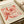 May include: Vintage-style art print featuring large coral and pink flowers in Matisse's paper cut-out style, displayed on cream paper with French exhibition text. Print sits on neutral fabric surface alongside rolled papers and ribbon, creating an elegant flat lay styling setup.