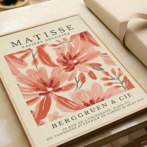 May include: Vintage-style art print featuring large coral and pink flowers in Matisse's paper cut-out style, displayed on cream paper with French exhibition text. Print sits on neutral fabric surface alongside rolled papers and ribbon, creating an elegant flat lay styling setup.