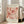 May include: Large framed poster leaning against white wall next to beige sofa in bright room with windows. Print features coral and pink abstract floral cutout shapes in Matisse's papier découpé style with cream background. French exhibition text at top and bottom in black letters. Light wooden frame, approximately 2-3 feet tall, positioned on light wood floors with natural sunlight streaming across scene.