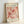 May include: Framed vintage-style exhibition poster featuring abstract floral cutout designs in coral, pink and peach tones on cream background. Light wooden frame displayed against white wall, showing French gallery text and 1953 date at bottom.
