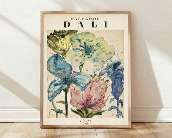 May include: Framed botanical poster featuring Salvador Dali's surrealist watercolor flowers in soft blues, yellows, and pink tones against cream background. The artwork shows delicate blooms with flowing, dreamlike qualities typical of Dali's style. Light wood frame sits on wooden floor against white wall with natural sunlight casting shadows across the scene.