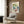 May include: A framed botanical poster featuring colorful vintage-style flowers in blues, greens, yellows, and pink with "Salvador Dali" text at top, displayed on wood-paneled wall above a beige upholstered armchair with geometric patterned pillow, brass floor lamp, and dark round side table with open book in a modern neutral-toned room setting.