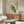 May include: Japanese woodblock-style owl print with traditional calligraphy and red seals, displayed in thin wooden frame above mid-century walnut credenza. Room features cream walls, white upholstered chair, oval glass coffee table with colorful abstract art underneath, and warm natural lighting creating soft shadows.