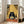 May include: Large framed poster print leaning against white wall next to beige sofa. Artwork shows black fluffy cat with wide eyes eating ramen noodles with chopsticks at orange table. Japanese-style kitchen background with bamboo mat walls, sake bottles, and traditional items. Text reads "RELYSTES FULL ENERGY" at bottom. Warm yellow and orange color palette with vintage illustration style.