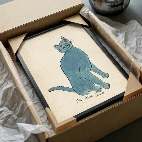 May include: Framed artwork showing a blue cat sitting upright with head tilted back, rendered in a simple illustrated style on cream-colored paper. The cat has pink inner ears and appears content with closed eyes. Text reads "One Blue Pussy" below the illustration. The black frame sits in an open cardboard shipping box with white tissue paper, alongside wooden dowels used for packaging protection.