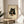 May include: Framed poster print displayed on wooden side table next to beige upholstered chair and plant. Artwork shows adorable black cat with large golden eyes holding chopsticks, eating sushi from a plate. Japanese-inspired illustration style with cream background, red accent seal, and natural wood frame. Soft natural lighting creates gentle shadows on neutral-toned wall.