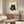 May include: Framed poster of a black cat with golden eyes holding chopsticks with sushi, sitting behind a plate of sushi rolls, displayed above a mid-century modern walnut credenza in a minimalist living room with cream walls, white curved chair, and glass coffee table with abstract art surface.