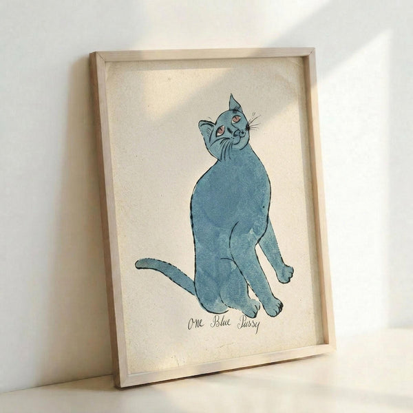 May include: Light wood frame displaying vintage-style illustration of blue cat sitting upright with head tilted back, rendered in soft blue watercolor with pink inner ears and whiskers, text below reads "One Blue Pussy" in cursive script, cream textured background, frame leaning against white wall