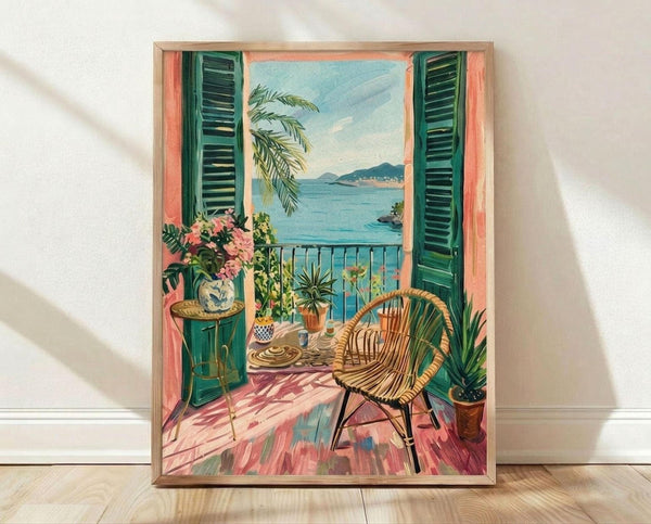 May include: Framed vintage-style Mediterranean balcony scene artwork leaning against white wall on light wood floor. Painting shows wicker chair on coral-pink tiled terrace with green shutters, tropical plants, and ocean view with distant mountains. Warm peachy-coral interior walls, decorative pottery, and palm fronds visible. Natural wood frame, soft window light creating shadows on wall.