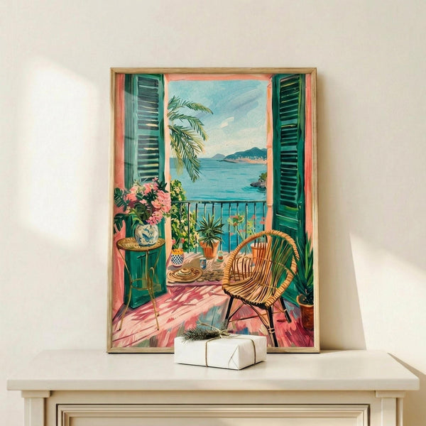 May include: Framed artwork displaying a Mediterranean balcony scene with green shutters, wicker chair, potted plants with pink flowers, and ocean view with distant mountains. The painting shows warm coral and turquoise tones with detailed interior elements like a small round table and decorative pottery. Artwork is positioned on a light wooden shelf next to a small wrapped gift with evergreen sprig.