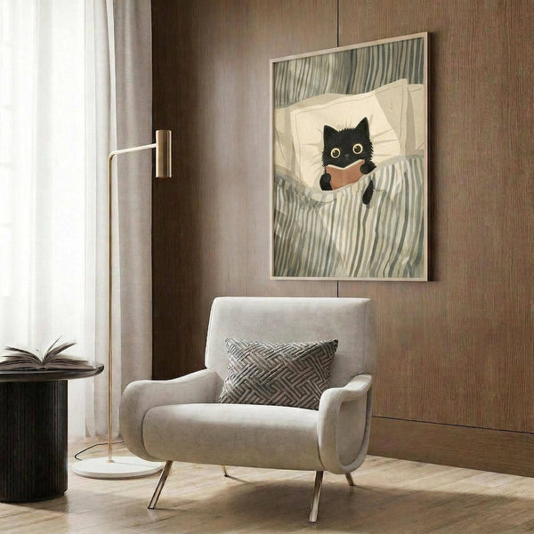 May include: Framed poster showing a black cat with wide yellow eyes reading a brown book while tucked in bed with white pillow and green striped bedding. Artwork displayed above a beige upholstered armchair with geometric patterned throw pillow in a modern living room with wood paneled walls, brass floor lamp, and side table with open book.