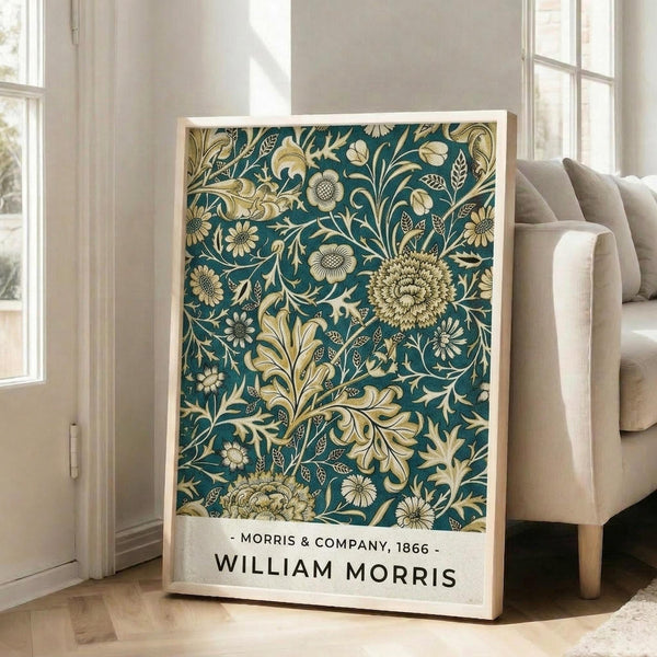May include: Framed poster with intricate teal and cream floral pattern featuring large chrysanthemums, flowing leaves, and decorative botanical motifs in William Morris Victorian style, displayed on light wooden floor against white wall near beige upholstered chair and tall windows with natural lighting