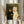 May include: Person holding framed vintage-style cat wedding artwork featuring black cat in golden collar and white cat in pink bow tie holding yellow bouquet against green background, displayed in light wood frame in bright interior with dried pampas grass and white curtains