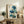 May include: Framed botanical artwork featuring blue poppies with Oriental calligraphy displayed on a rustic wooden sideboard alongside books, ceramic vases, and a fern plant in a neutral-toned living room setting with beige chair visible in foreground