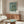 May include: Van Gogh's Almond Blossom artwork poster in wooden frame, showing white flowering branches against turquoise blue background, displayed above mid-century modern walnut credenza with brass hardware. Modern living room setting features cream sculptural chair, glass-top oval coffee table, white table lamp, and brass floor lamp on light wooden floors.