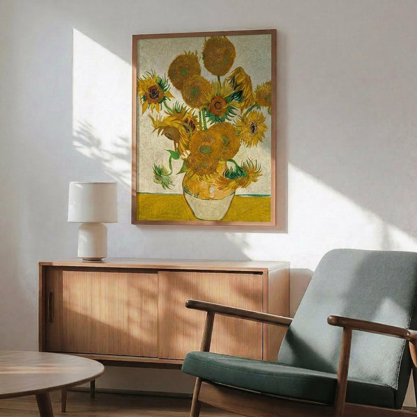 May include: Van Gogh's Sunflowers painting reproduction in wooden frame hanging above mid-century modern wood credenza with white ceramic lamp. Sage green upholstered armchair with wooden arms sits nearby. Bright sunlight casts dramatic shadows across white wall in minimalist living room setting.