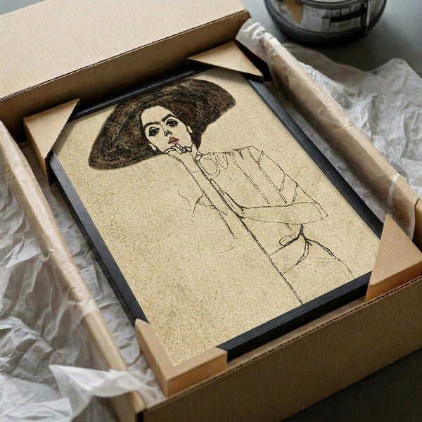 May include: Framed artwork in black frame being unpacked from cardboard shipping box with protective wrapping. The print shows a sketched portrait of a woman with dark voluminous hair wearing a light-colored blouse, drawn in brown lines on cream-colored paper. Wooden dowels and tissue paper visible around the package on white surface.