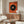 May include: Abstract art print with orange background and large black circle containing concentric colored rings in blue and yellow, displayed above walnut credenza in modern living room with white curved chair, brass floor lamp, and round glass coffee table