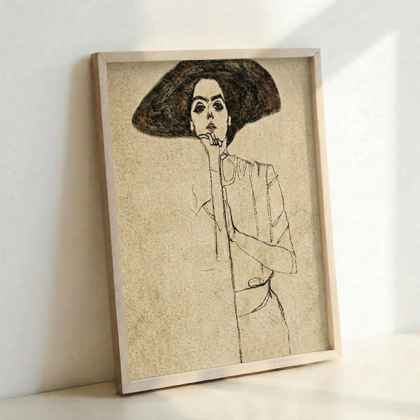 May include: Framed art print leaning against white wall showing minimalist line drawing of woman with large dark hat and thoughtful pose, hand near chin. Sketch style artwork on beige textured background in light wood frame, creating vintage artistic wall decor in clean modern interior setting.