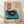 May include: Vintage-style poster featuring a turquoise record player with black vinyl and red center label, displayed in light wooden frame against cream textured background. Japanese characters in red rectangle at top, with additional red text block. Poster shows weathered, retro aesthetic with teal ink spots at bottom, leaning against white wall on light wood floor.