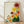 May include: Framed botanical poster print leaning against white wall on light wood floor. Features stylized sunburst flowers in vibrant yellow, orange, pink and red with radiating petal patterns, alongside green foliage on cream background. Natural wood frame, soft lighting creates gentle shadows on textured white wall.