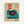 Framed vintage-style poster featuring a turquoise record player with black vinyl and orange center label on cream background. Red rectangular banner with white Japanese characters sits above the turntable, with vertical Japanese text on left side and paragraph of red text on right. Two small teal circular stamps appear at bottom. Natural wood frame against white wall.