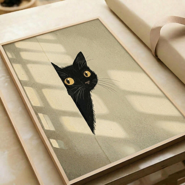 May include: Framed art print showing a black cat with bright yellow eyes peeking around what appears to be a corner or doorway, rendered in muted beige and olive green tones with soft shadowing. The wooden-framed piece sits on a light wooden surface next to rolled paper or fabric in neutral cream colors, creating a warm, minimalist styling scene.