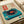May include: Vintage-style poster print featuring a turquoise blue record player with black vinyl record and red center label, displayed in white matted frame on light wooden surface. Japanese characters appear in red box in upper left corner with accompanying text. Retro illustration has weathered, aged paper texture with small blue ink spots as decorative elements.