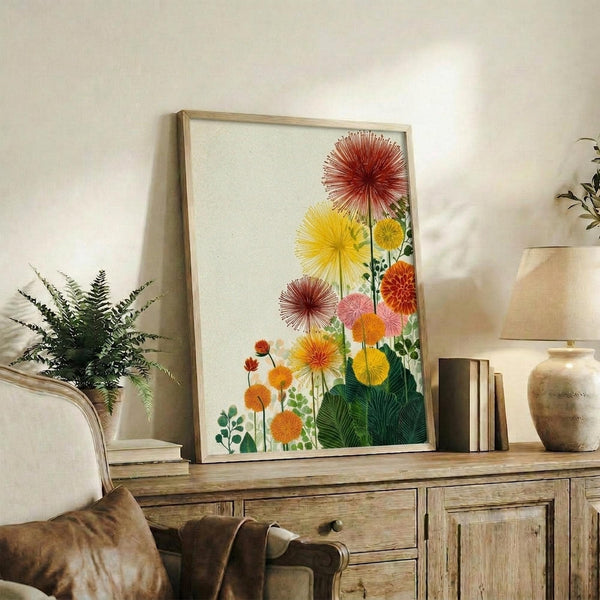 May include: Framed botanical art print featuring vibrant sunburst-style flowers in red, yellow, orange, and pink tones with green foliage, displayed on rustic wooden sideboard alongside fern plant, books, ceramic vase, and table lamp in neutral-toned living room setting with beige chair and throw pillows.