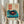 May include: Person holding framed vintage-style poster featuring turquoise record player with red vinyl record, Japanese text in red box, beige textured background, dried wheat stems visible to left, soft natural lighting near window with curtains, cream colored clothing sleeves visible